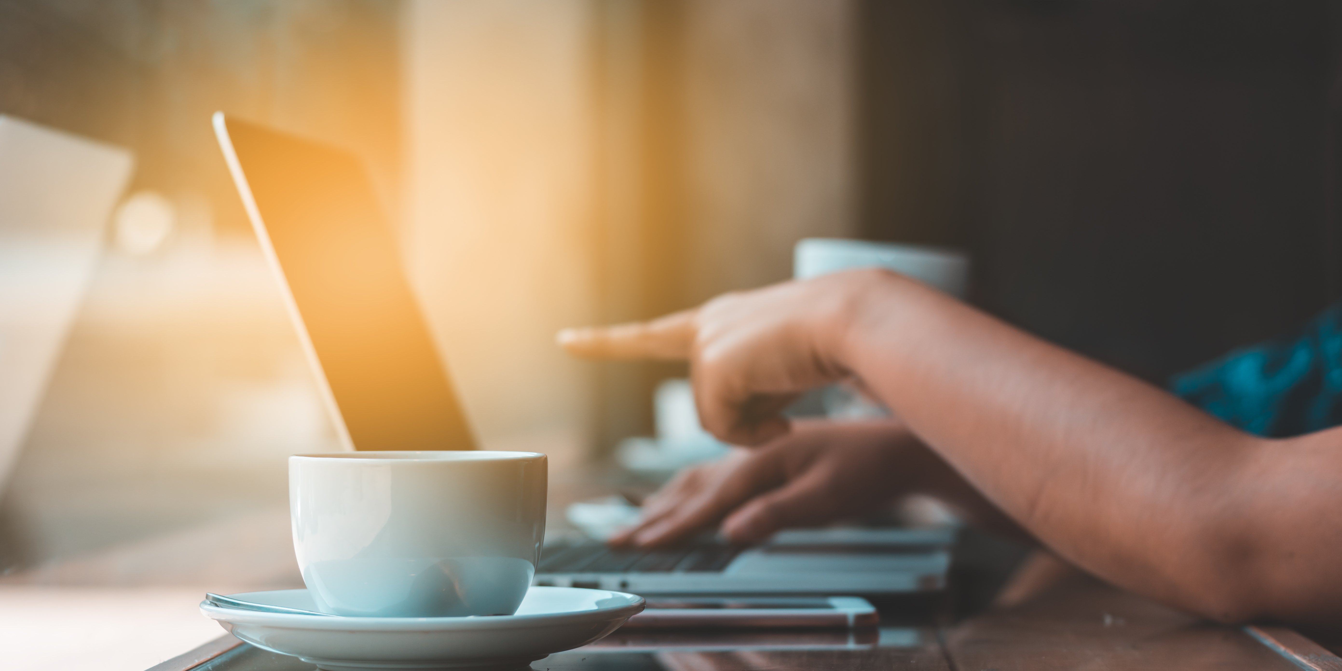 Tasse an Laptop mit Hand die auf Bildschirm zeigt