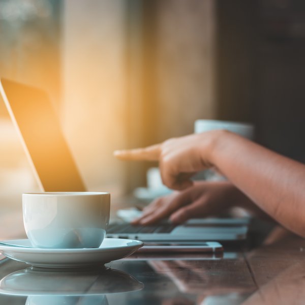 Tasse an Laptop mit Hand die auf Bildschirm zeigt
