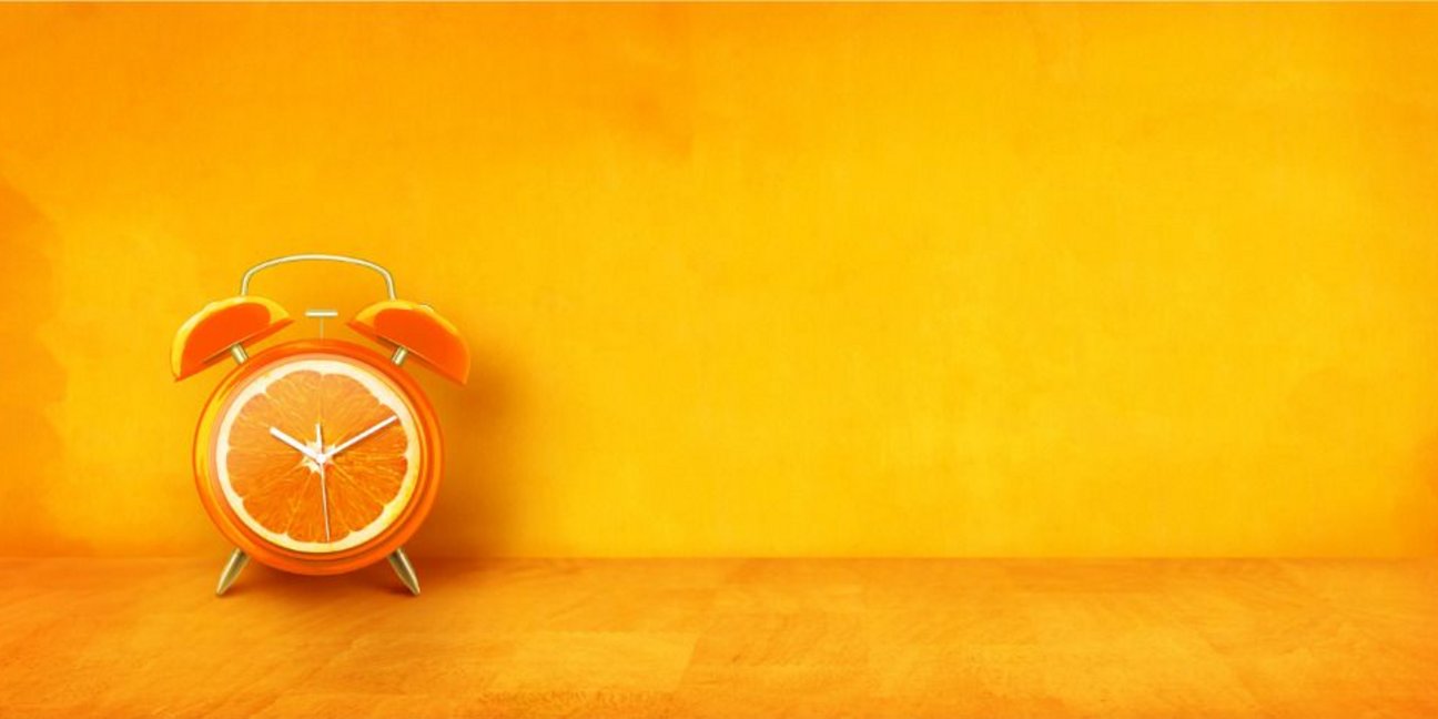 Eine Orange als Wecker vor orangefarbenem Hintergrund
